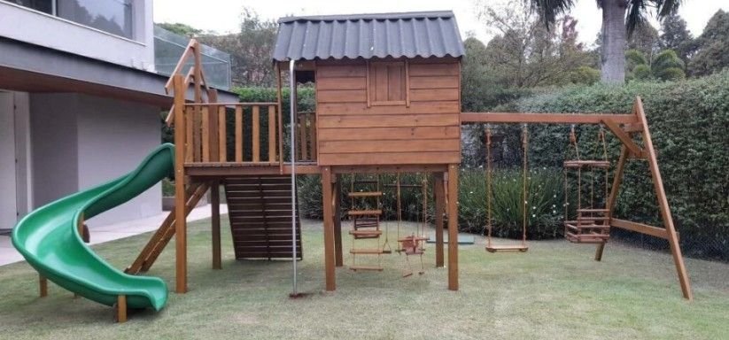 Casinha suspensa de madeira com escorregador curvo verde, cano de bombeiro e balanços